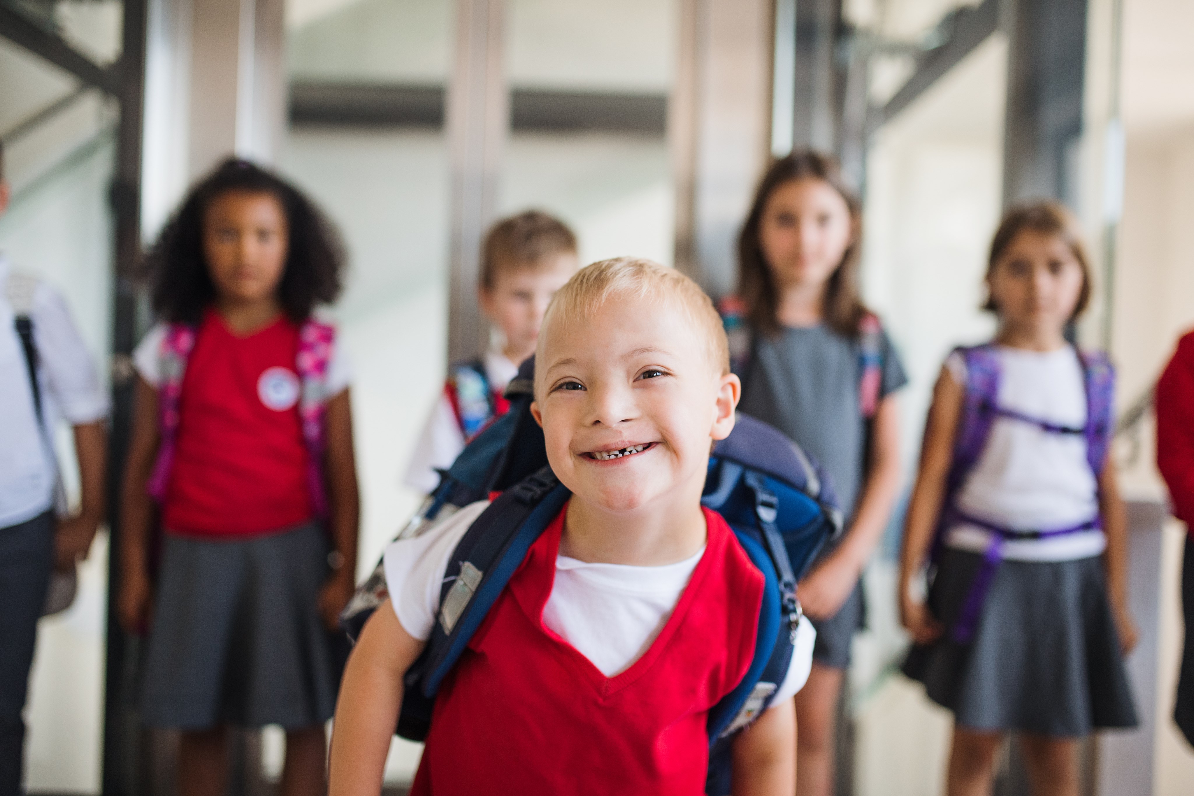 Gruppe von Kindern mit Rucksäcken, eines davon mit Trisomie 21 lächelt