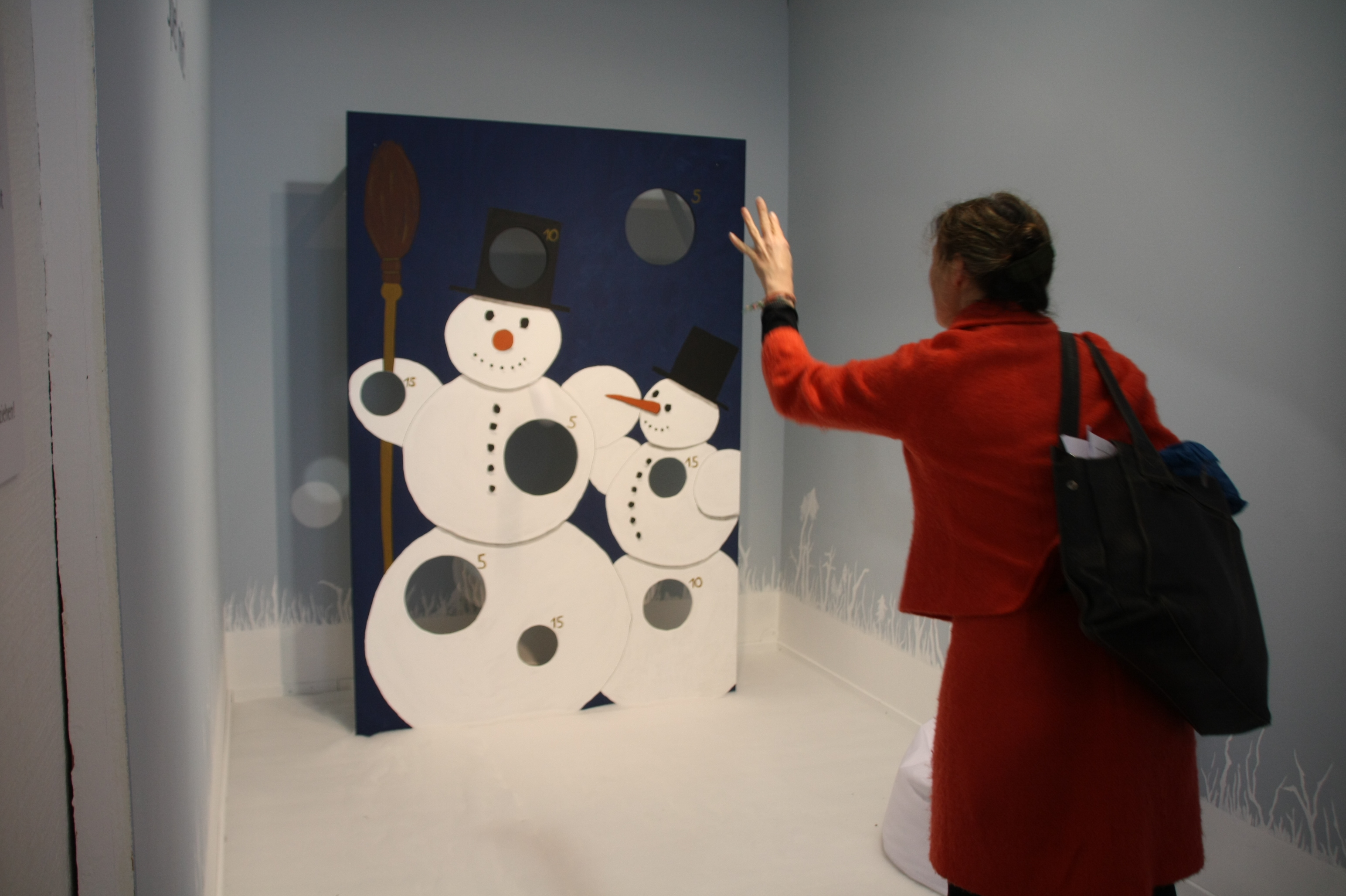 Eine Wand mit bei Abbildungen von Schneemänner; darin sind große Löcher, durch die man (Schnee-)Bälle werfen kann.