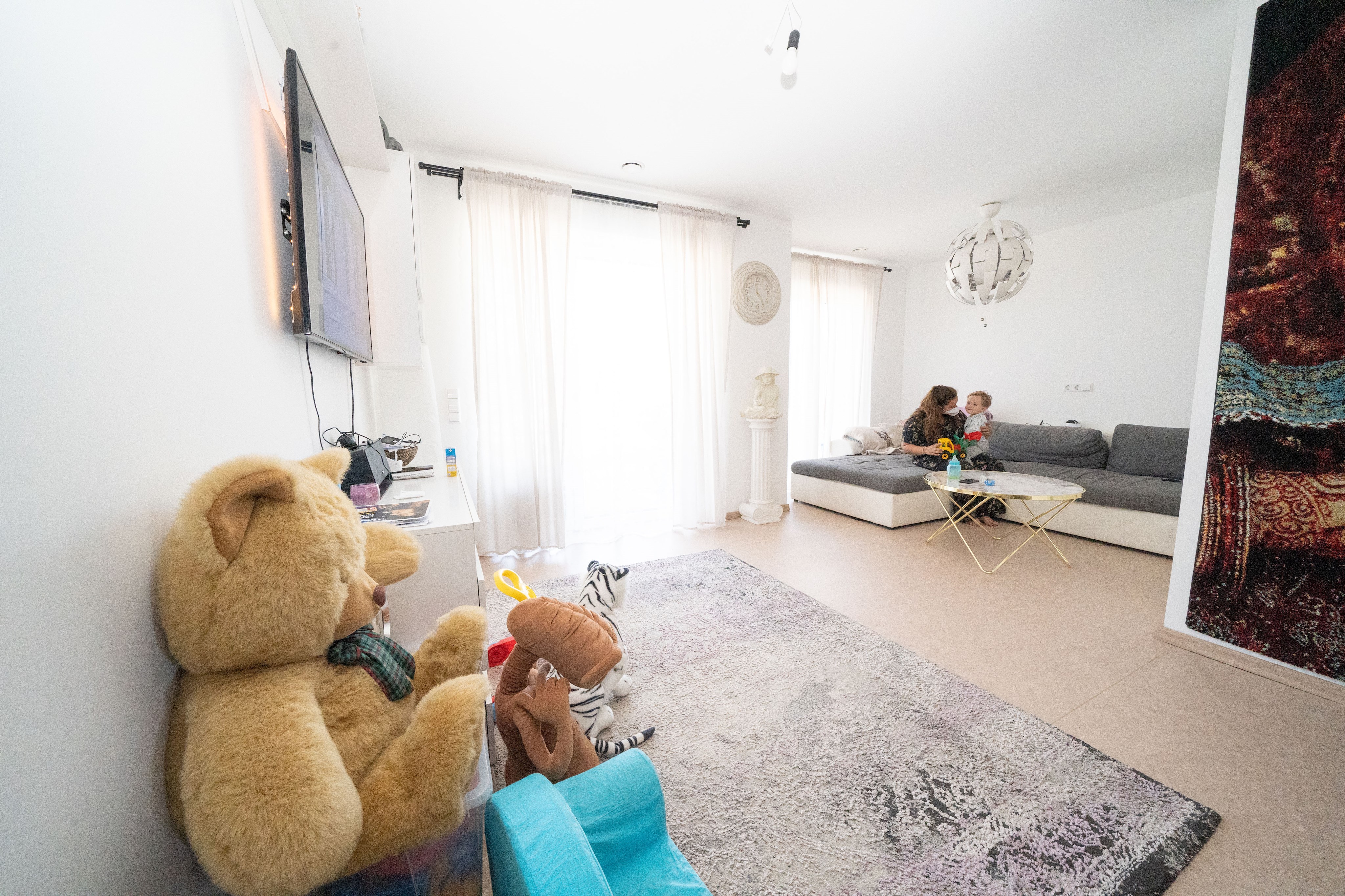 Foto: ein helles Wohnzimmer, auf einem Sofa spielt eine Frau mit ihrem Kind