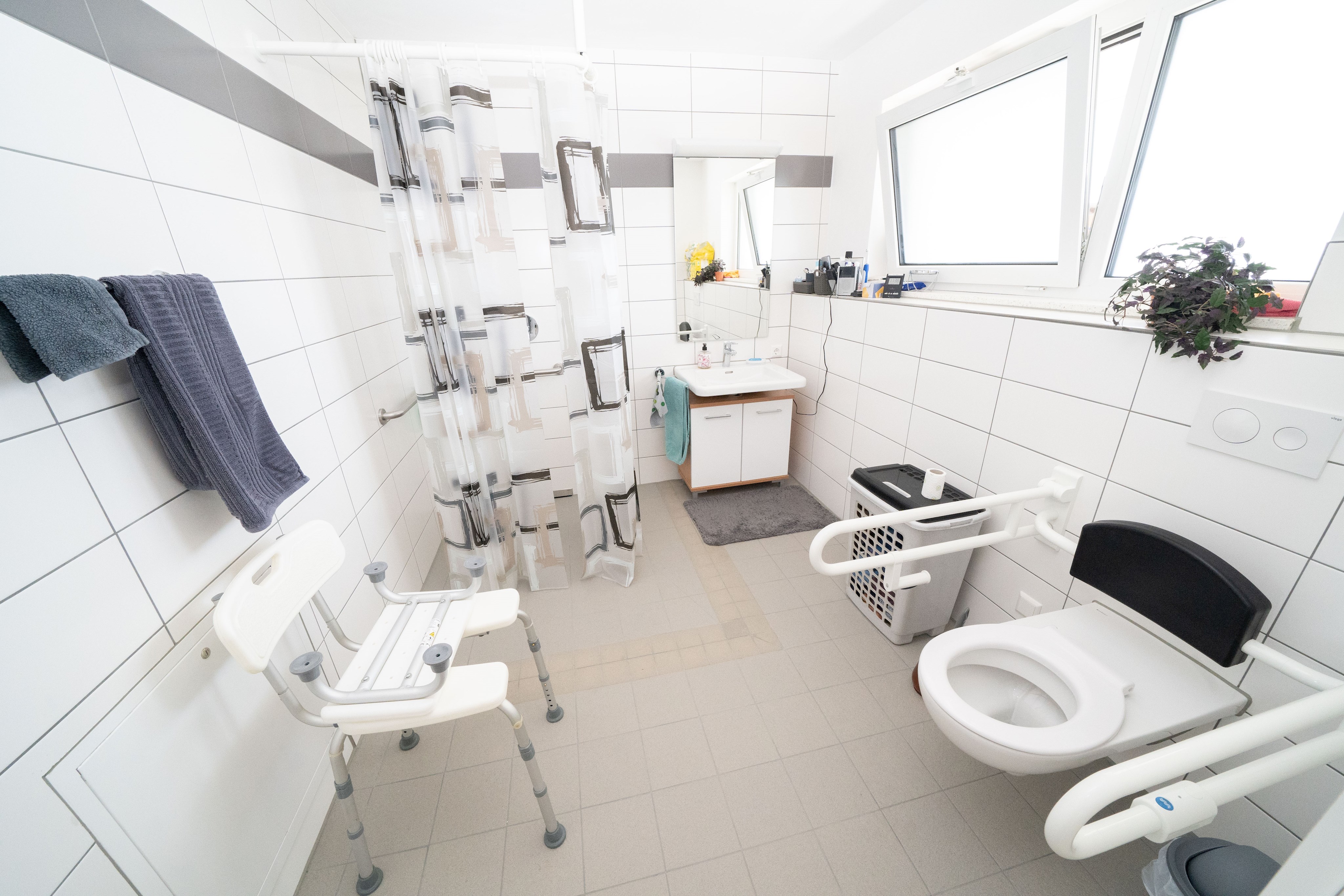 Foto: ein Badezimmer mit ebenerdiger Dusche und einer Toilette mit Handgriffen zum Festhalten an beiden Seiten