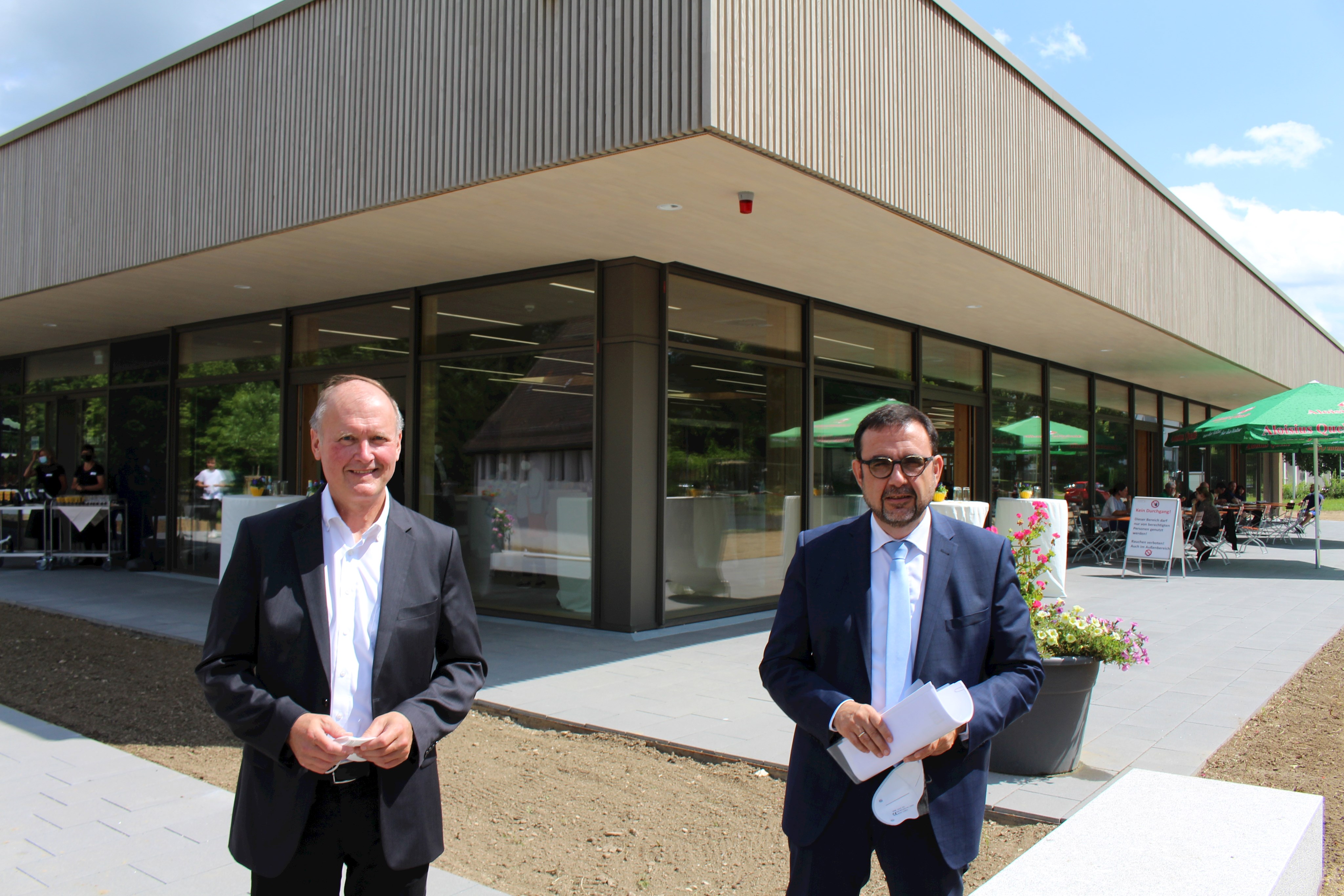 Der stellvertretende Verwaltungsratsvorsitzende der Bezirkskliniken Schwaben, Bezirksrat Dr. Johann Popp (links), mit dem bayerischen Gesundheitsminister Klaus Holetschek vor dem Neubau auf dem Gelände des Günzburger Bezirkskrankenhauses, in dem unter anderem die Speisenversorgung, die Mehrzweckhalle und umfangreiche technische Anlagen integriert worden sind.